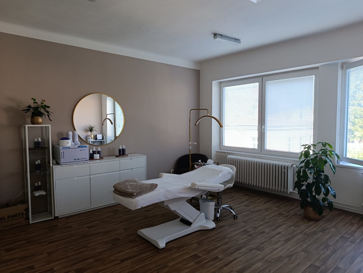 Interiér salonu Miracle Beauty s kosmetickým lehátkem, kulatým zrcadlem a velkými okny